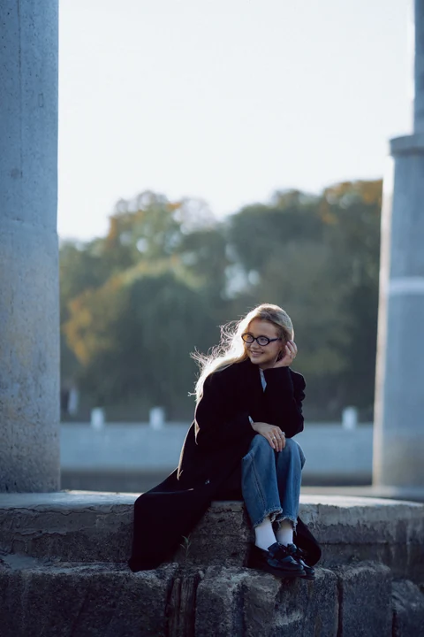 Девушка в очках улыбается, сидя на каменных ступенях